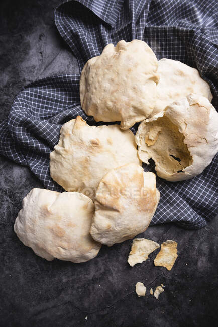 Pita bread on a tea towel, one broken open — Stock Photo
