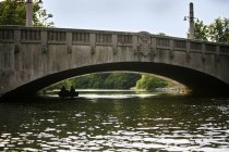 Friends pedaling boat below arch bridge — Stock Photo