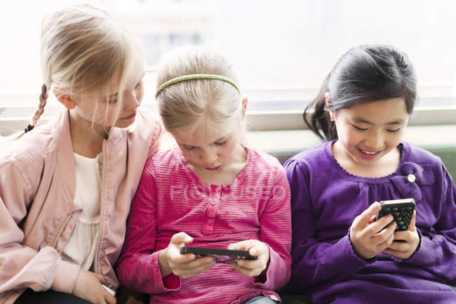 Three girls sitting with smartphones — Stock Photo