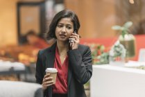 Young asian business woman talking on cellphone in modern office — Stock Photo