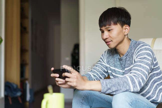 Jeune adulte asiatique homme en utilisant smartphone à la maison — Photo de stock