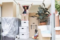 Portrait playful girl jumping up from behind cardboard boxes in moving van — Stock Photo
