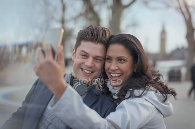 Smiling couple taking selfie with camera phone in urban park — Stock Photo