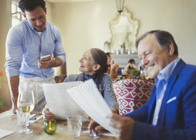 Waiter taking order from senior couple with menus at restaurant table — Stock Photo