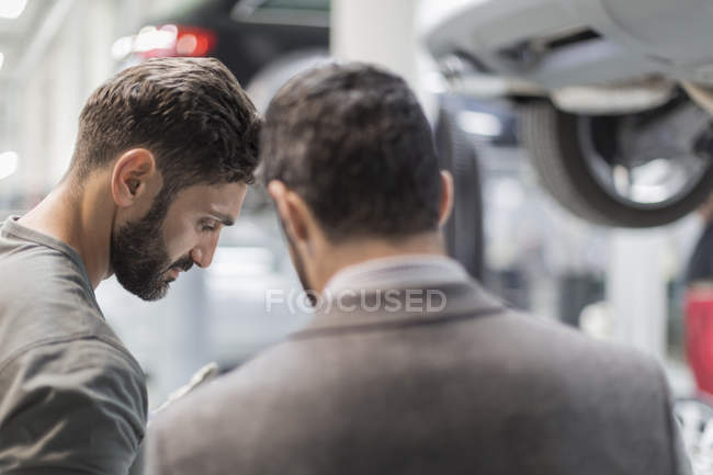 Male mechanic and customer talking, looking down in auto repair shop — Stock Photo