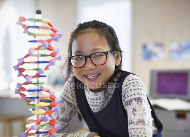 Portrait smiling, confident girl student next to DNA model in classroom — Stock Photo