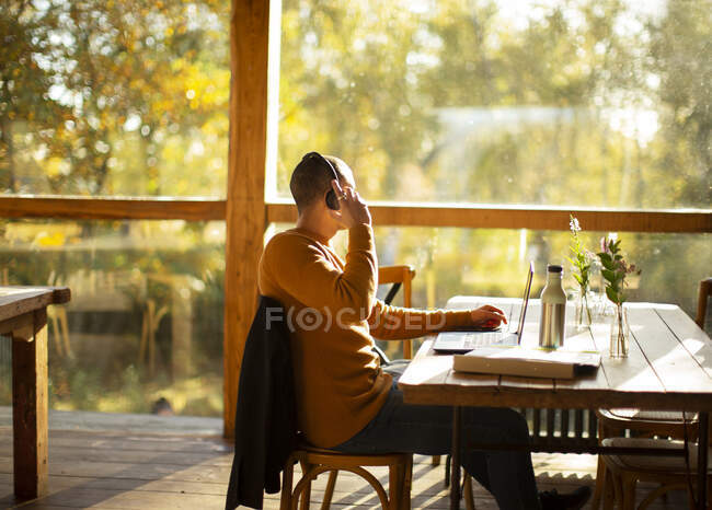 Businessman with headphones working at laptop in sunny autumn cafe — Stock Photo