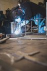 A blacksmith wears safety gear and is welding a metal construction in a metalsmith's workshop. — Stock Photo