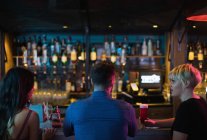 Friends enjoying alcoholic drinks at counter in bar — Stock Photo