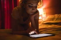 Woman lying and using digital tablet on bed in bedroom — Stock Photo