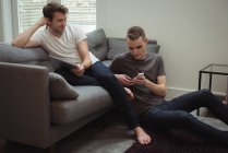 Gay couple using digital tablet and mobile phone in living room at home — Stock Photo
