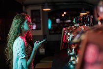 Beautiful woman using mobile phone at counter in bar — Stock Photo