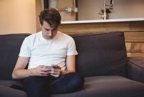 Man sitting on sofa using mobile phone in living room at home — Stock Photo