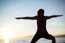 Back view of Woman performing yoga on beach during sunset — Stock Photo