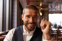 Portrait close up of a smiling young Caucasian man sitting at a table inside a cafe. Digital Nomad on the go. — Stock Photo
