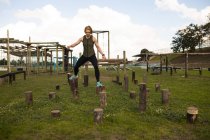 Front view of a young Caucasian woman jumping between wooden posts at an outdoor gym during a bootcamp training session — Stock Photo