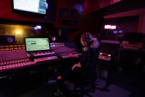 Side view of a young Caucasian female sound engineer sitting and working at a mixing desk in a recording studio surrounded by equipment — Stock Photo