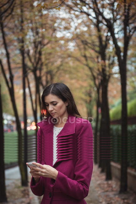 Businesswoman using phone standing on the pathway with trees — Stock Photo