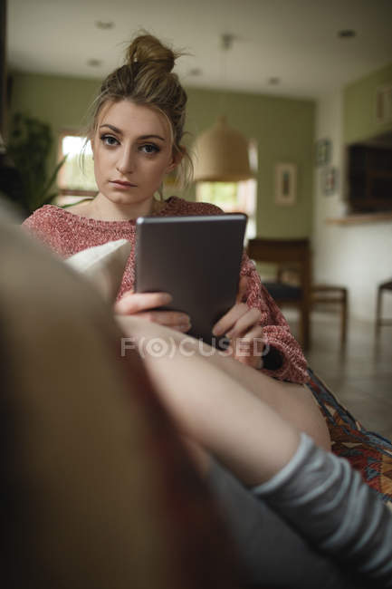 Woman sitting and using digital tablet on couch in living room at home — Stock Photo