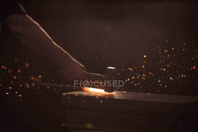Hand of blacksmith working on iron rod with hammer in workshop — Stock Photo