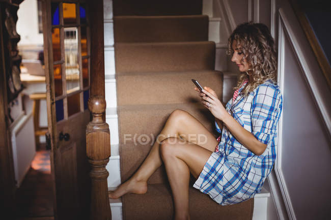 Beautiful woman sitting on staircase and using mobile phone at home — Stock Photo