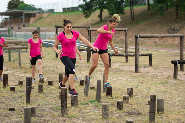 Multi-ethnic group of women all wearing pink t shirts at a boot camp training session, exercising, balancing and walking across logs. Outdoor group exercise, fun healthy challenge. — Stock Photo