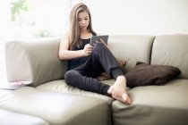 Teenage girl using digital tablet on couch at home — Stock Photo