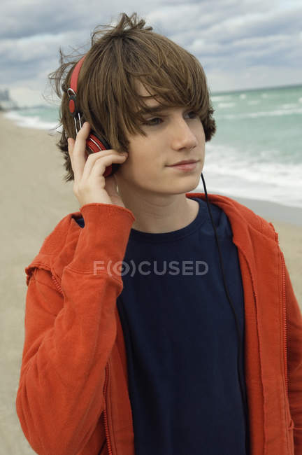 Close-up of teenage boy listening to music with headphones on sea beach — Stock Photo