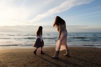 Rear view of mother with daughter standing at beach against sky with clouds — Stock Photo