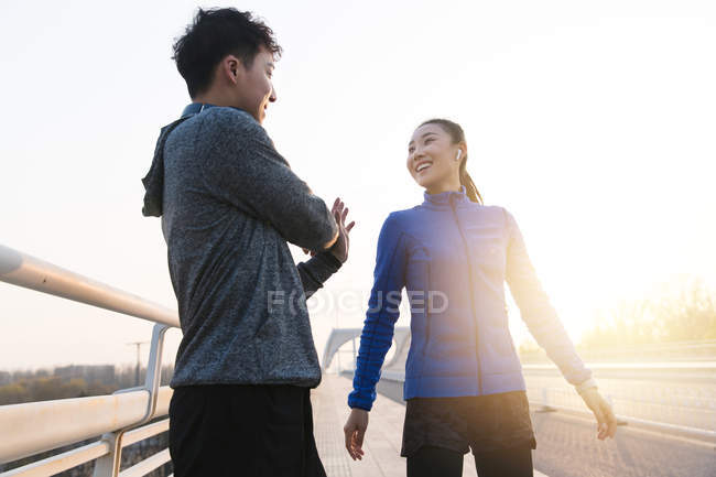 Low angle view of young asian joggers stretching together during workout in bridge in the morning — Stock Photo