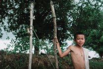 LAOS, 4000 ISLANDS AREA: Shirtless  boy standing in nature near two wooden poles and smirking. — Stock Photo