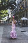 Eccentric woman in colorful pink costume speaking on smartphone while walking along summer street — Stock Photo