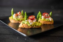 Closeup delicious small sandwiches with shrimp and vegetables placed on ceramic plate on black table in cafe on black background — Stock Photo