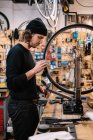 Side view of young male master examining tire on bike wheel while working in professional repair service workshop — Stock Photo
