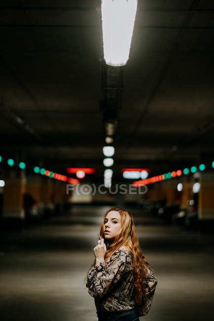 Pretty redhead woman smoking while walking on blurred parking lot — Stock Photo