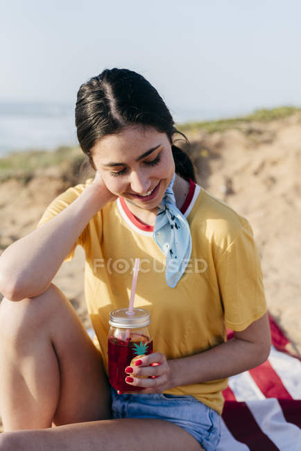 Teenage girl with drink sitting on sand — Stock Photo