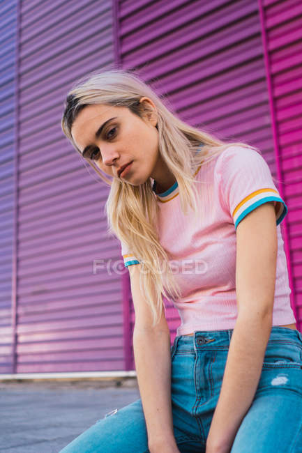 Blonde woman posing sitting against multicolored wall and looking at camera — Stock Photo