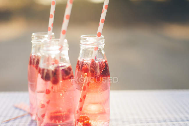 Bottles with fresh fruit drink and drinking straws on table outdoors — Stock Photo