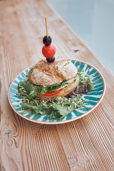 Delicious vegetarian sandwich with tomatoes, onion, lettuce, olives and cherry tomato on bright plate on wooden table in restaurant — Stock Photo