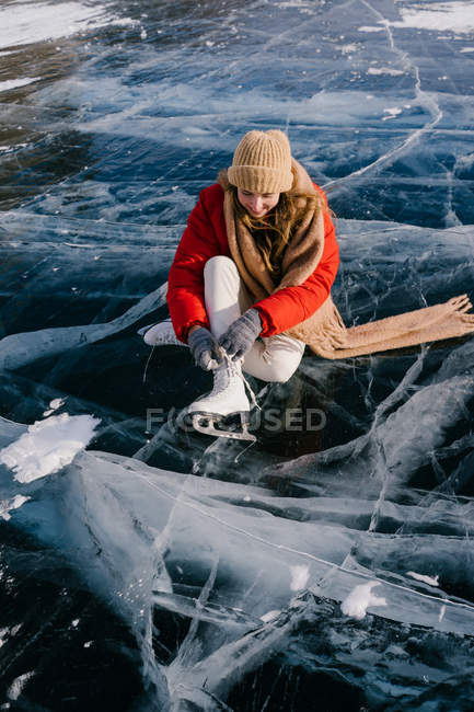 Woman sitting on frozen river and tying the shoelaces — Stock Photo