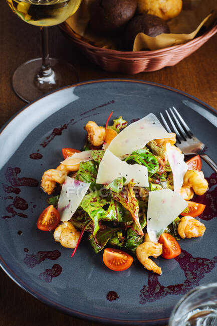 From above closeup of delicious salad with fresh vegetables and leaves with shrimps and cheese served on black plate with sauce — Stock Photo