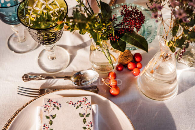 Angle élevé de table de fête servie avec des verres en cristal serviette de coutellerie sur l'assiette près de bouquet de fleurs fraîches pour mariage et carte de menu — Photo de stock