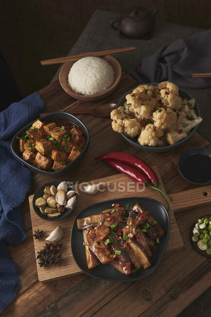 Mala tofu e yuxiang, pratos chineses vegan, acompanhado por uma tigela de arroz, couve-flor, molho de soja e um bule japonês em cima de uma mesa de madeira decorada com tecidos — Fotografia de Stock