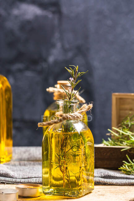 Glass bottle of essential oil with rosemary twigs and burning organic wooden candle on gray table — Stock Photo