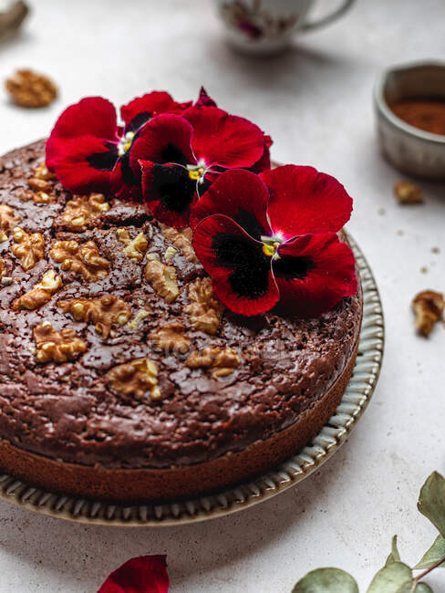 From above of sweet chocolate cake garnished with red flowers and walnuts served on table — Stock Photo