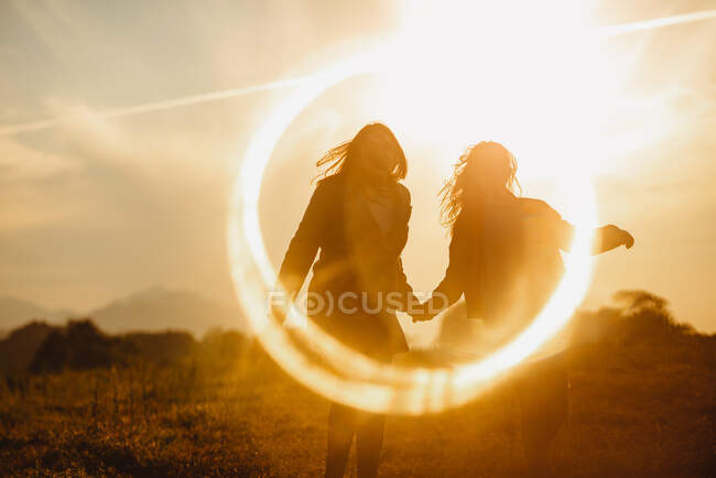 Girlfriends holding hands gently standing in lens flare of sunset light in nature — Stock Photo