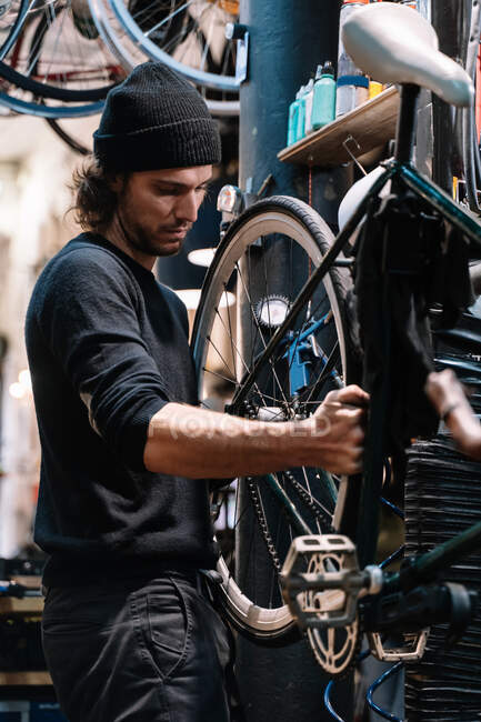 Side view of young male master examining tire on bike wheel while working in professional repair service workshop — Stock Photo