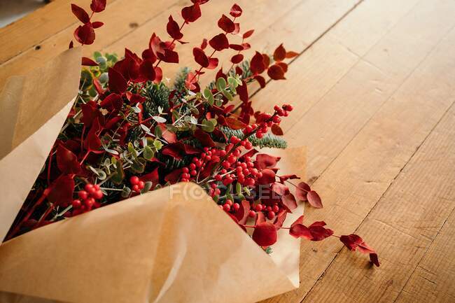From above of festive stylish decorative Christmas bouquet with twigs of eucalyptus and bright red branches with berries placed on wooden table in room — Stock Photo