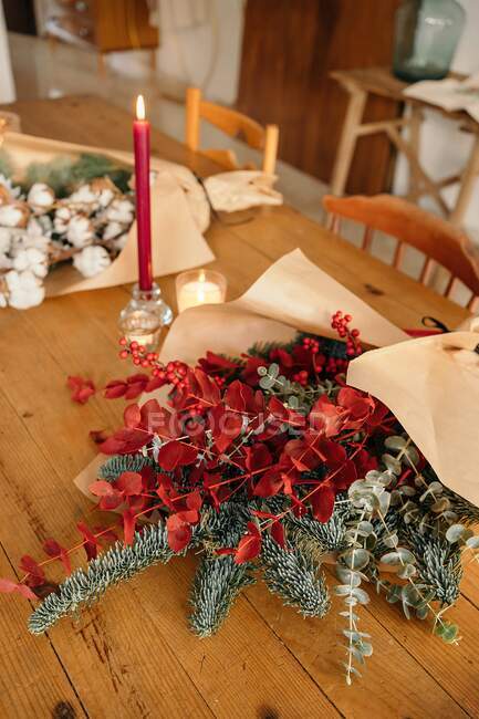 From above of festive stylish decorative Christmas bouquet with twigs of eucalyptus and bright red branches with berries placed on wooden table with candles in room — Stock Photo