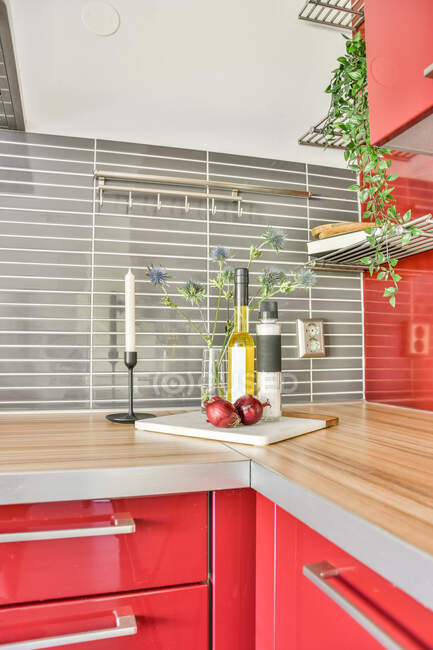 Bottle of oil and salt placed on red counter with candle and flowers in modern kitchen — Stock Photo